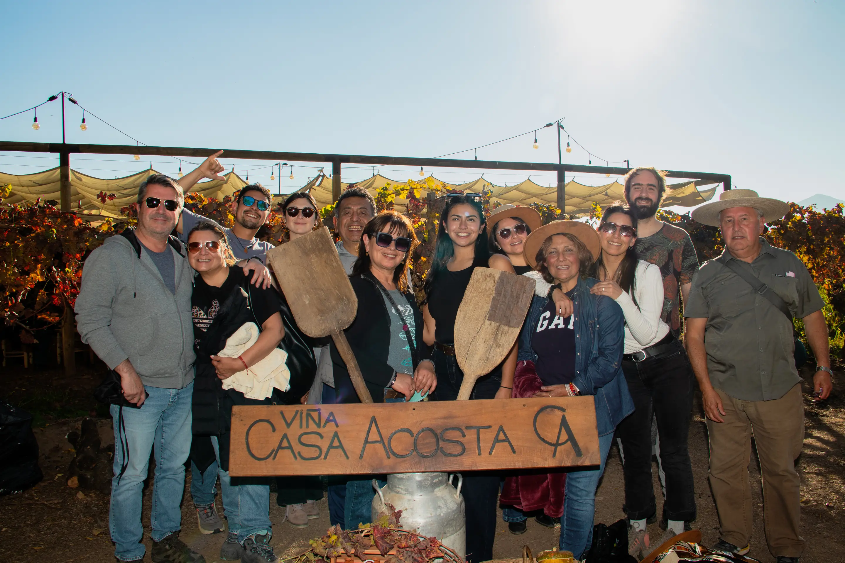 Grupo de visitantes posando con el cartel tallado de Viña Casa Acosta entre las parras del viñedo en otoño, a contraluz del atardecer